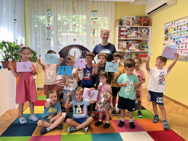 Обща снимка на деца с авторката н акнигата за Благо и Ая звездна одисея Обща снимка на много деца на фона на детска градина с авторката на звездна одисея Галя ненчева