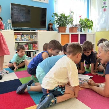 Деца са се скупчили около книга и авторката им показва сателити и космически обекти