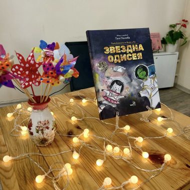 детската книга за Космоса Звездна одисея изложена на маса с малки лампички около нея