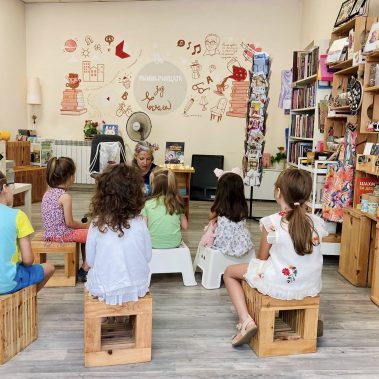 Деца са седнали на столчета и слушат как авторката Галя Ненчева чете своята детска книжка Звездна одисея