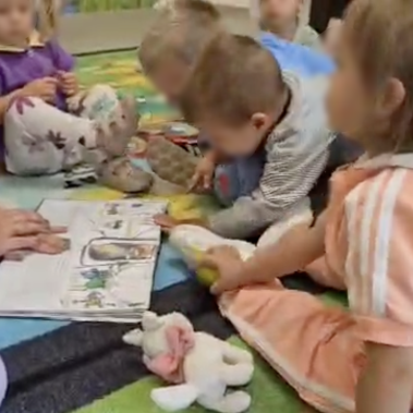 Малки деца са се скупчили над книга за Космоса и авторката им показва илюстрациите и им задава въпроси