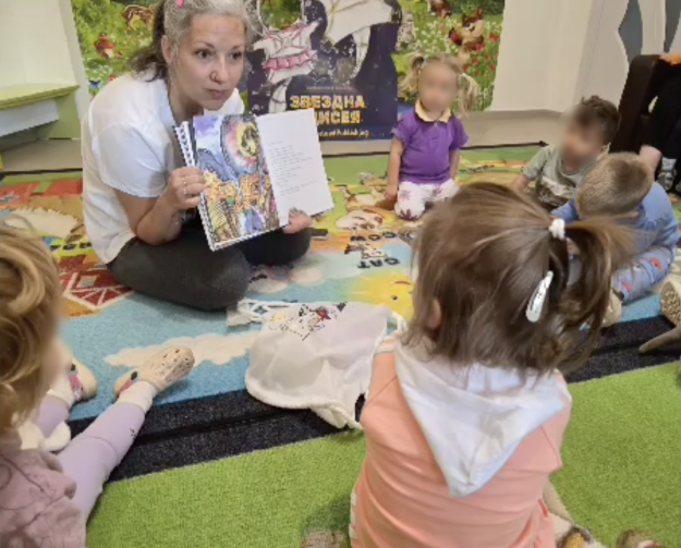 Галя Ненчева показва ярка илюстрация на Слънцето и обеснява на децата историята на Ая и Благо